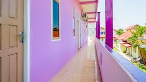 A corridor with a purple wall, a tiled floor, and a balcony with a railing. - OYO Life 2745 Nabeza House (Mandau)