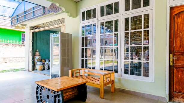 A room with a wooden table and bench, large windows, and a door. - OYO Life 2745 Nabeza House (Mandau)