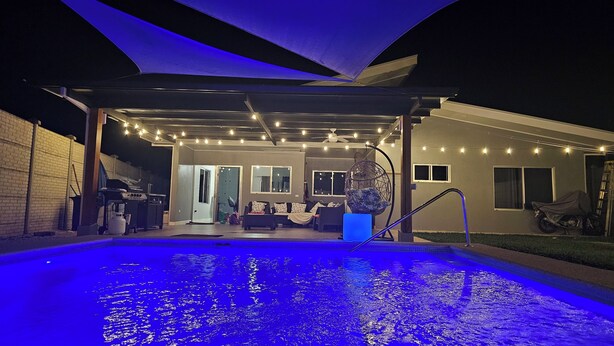 Un espace piscine extérieur doté d’un coin salon couvert, de guirlandes lumineuses et d’un ventilateur de plafond.