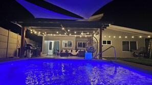 Un espace piscine extérieur doté d’un coin salon couvert, de guirlandes lumineuses et d’un ventilateur de plafond.