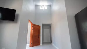 Un couloir étroit aux murs blancs, avec une porte en bois sur la gauche et une porte fermée au fond.