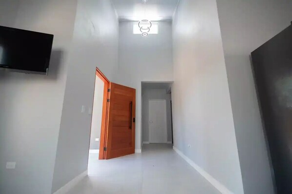 Un couloir étroit aux murs blancs, avec une porte en bois sur la gauche et une porte fermée au fond.