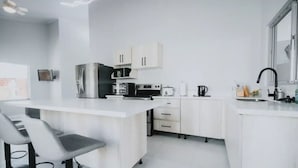 Une cuisine moderne avec des meubles blancs, un îlot central et un coin bar avec des tabourets.