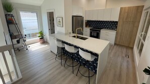 A modern kitchen with a central island, white cabinets, and a wooden wardrobe. - Location! New, Modern Townhouse Steps from 124 Street! (Edmonton)
