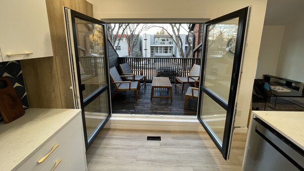 A modern kitchen with a sliding glass door leading to an outdoor patio with a wooden deck and seating area. - Location! New, Modern Townhouse Steps from 124 Street! (Edmonton)
