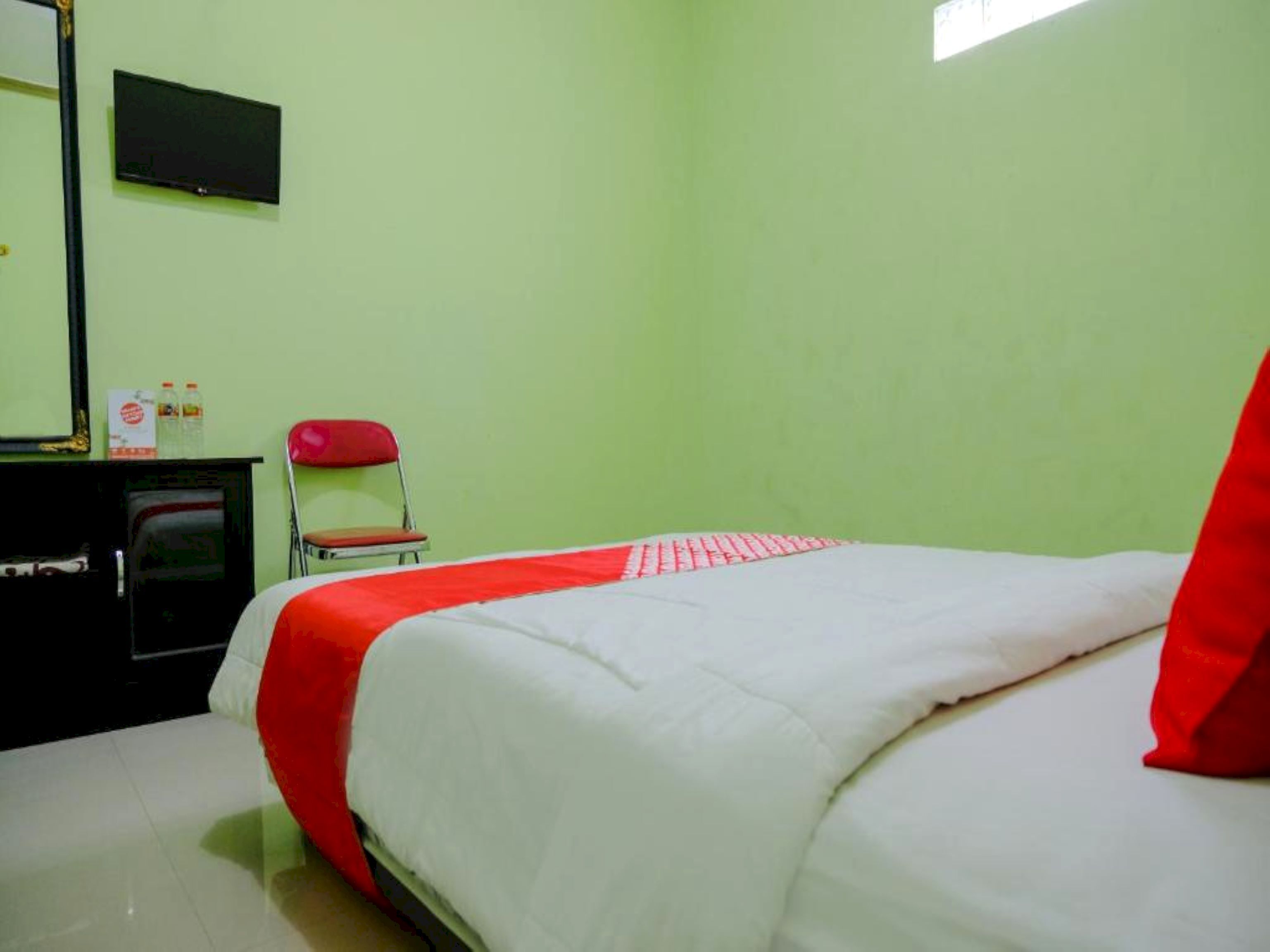 Een kamer met een bed, een stoel, een flatscreen-tv en een klein tafeltje met flessen.