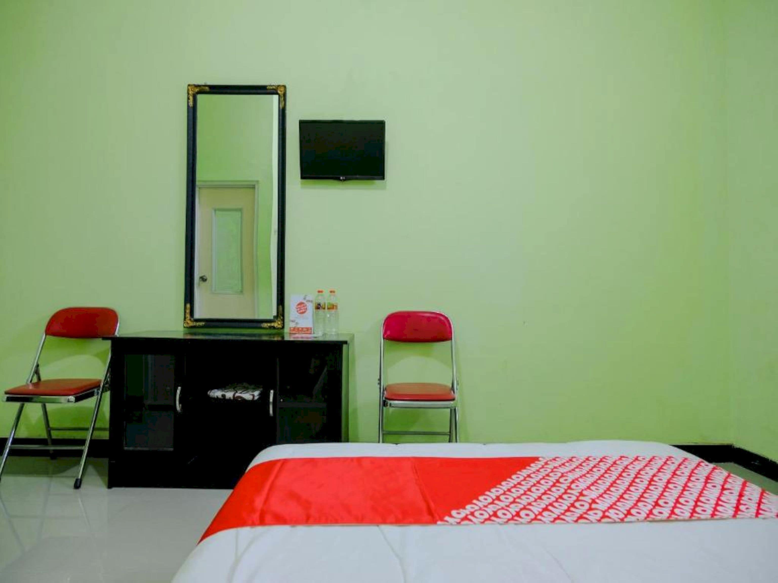 A hotel room with a bed, two red chairs, a black dresser, a mirror, and a small framed picture on the wall.