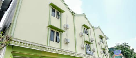 Un edificio de varios pisos con fachada verde, varias ventanas y unidades de aire acondicionado.