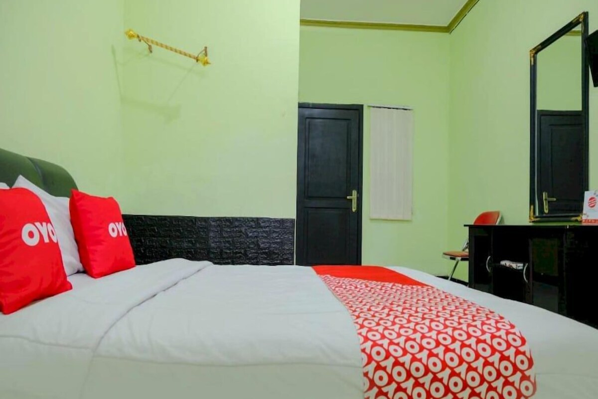 Una habitación de hotel con cama, escritorio, silla, puerta y espejo.