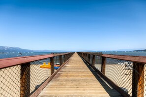 A wooden pier leading to a beach with a clear view of the sea and distant mountains.