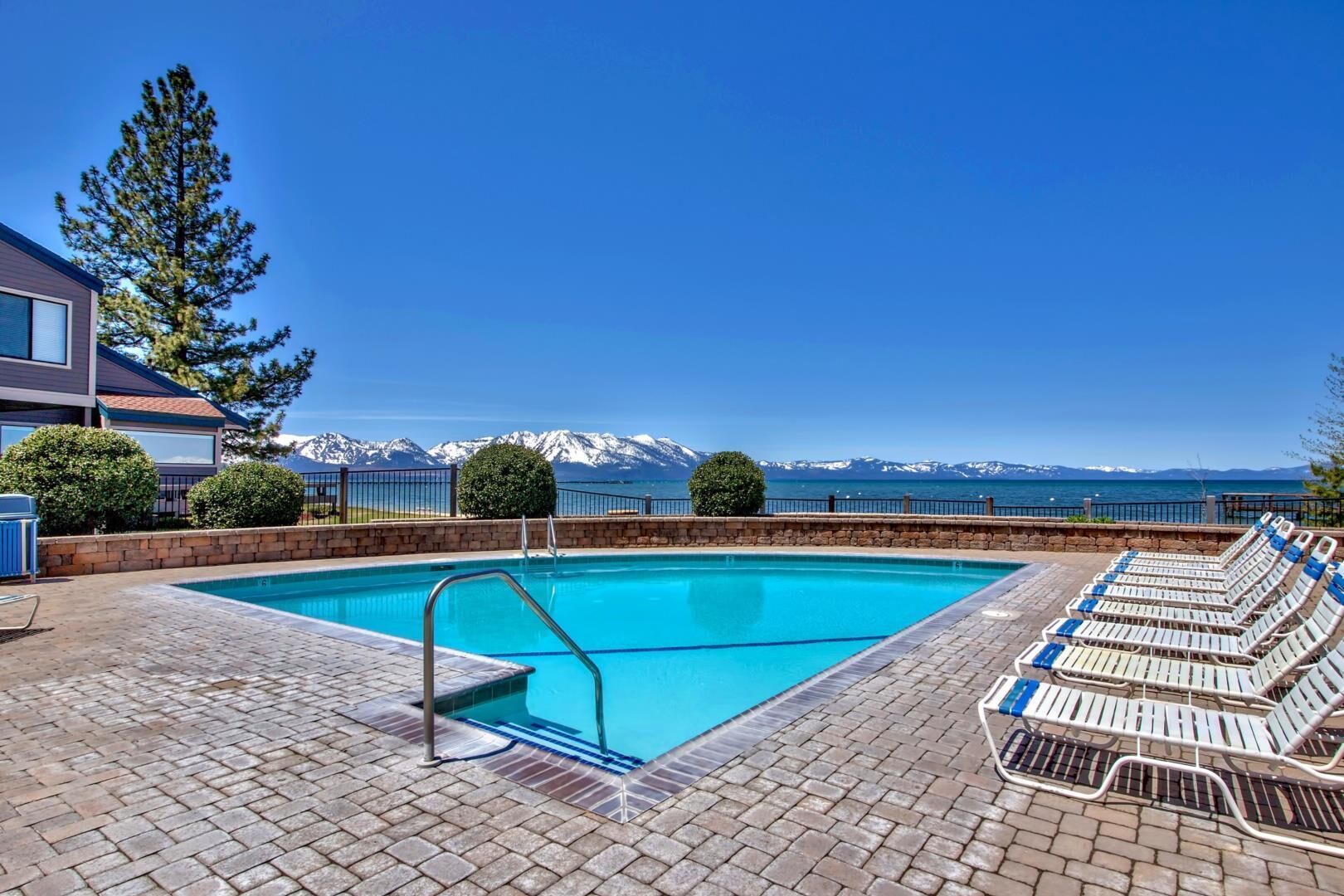 Seasonally available Outdoor pool framed by manicured hedges and stunning lake and mountain views, perfect for relaxing under clear skies on a beautiful day.