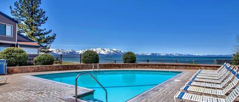 Seasonally available Outdoor pool framed by manicured hedges and stunning lake and mountain views, perfect for relaxing under clear skies on a beautiful day.