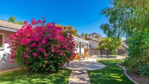 A residential property with a well-maintained lawn, a patio area with outdoor furniture, and a large flowering bush. - Beautiful, Sunshine Paradise Escape! (Phoenix)