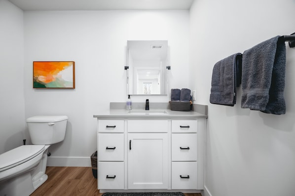 A modern bathroom with a white toilet, a white vanity with a mirror, and two towels hanging on the wall.