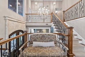 Una amplia escalera con barandales decorados, un candelabro y un sofá estampado con un cojín.