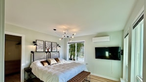 A bedroom with a large bed, a bench, a TV, and a window.