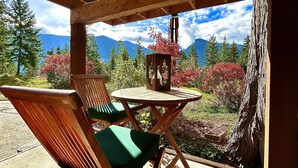 Um deck de madeira com mesa e cadeiras, com vista para uma paisagem montanhosa com árvores e céu claro.
