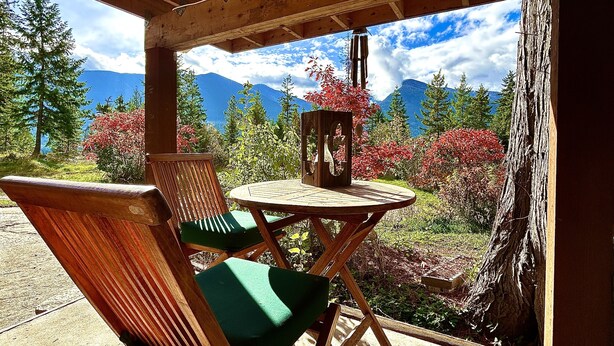 A wooden deck with a table and chairs, overlooking a mountainous landscape with trees and a clear sky.