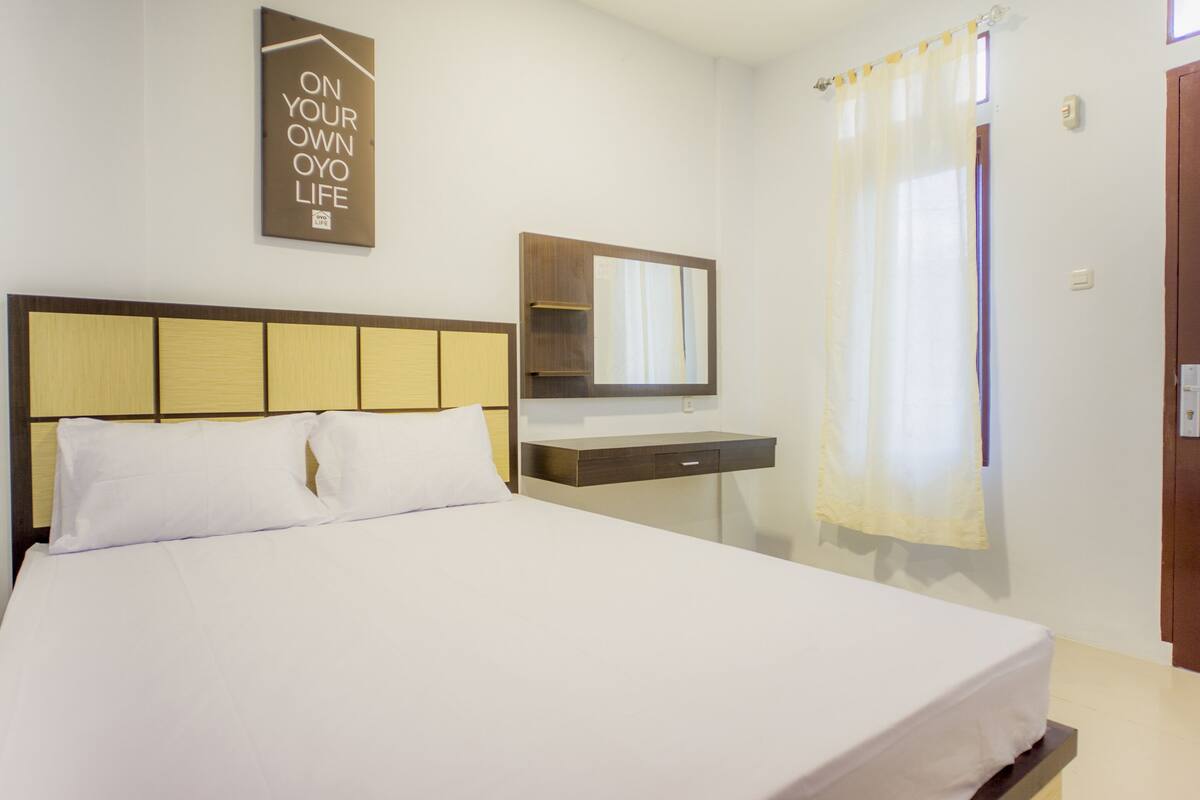 A hotel room with a bed, a bedside table, a mirror, and a window with curtains.