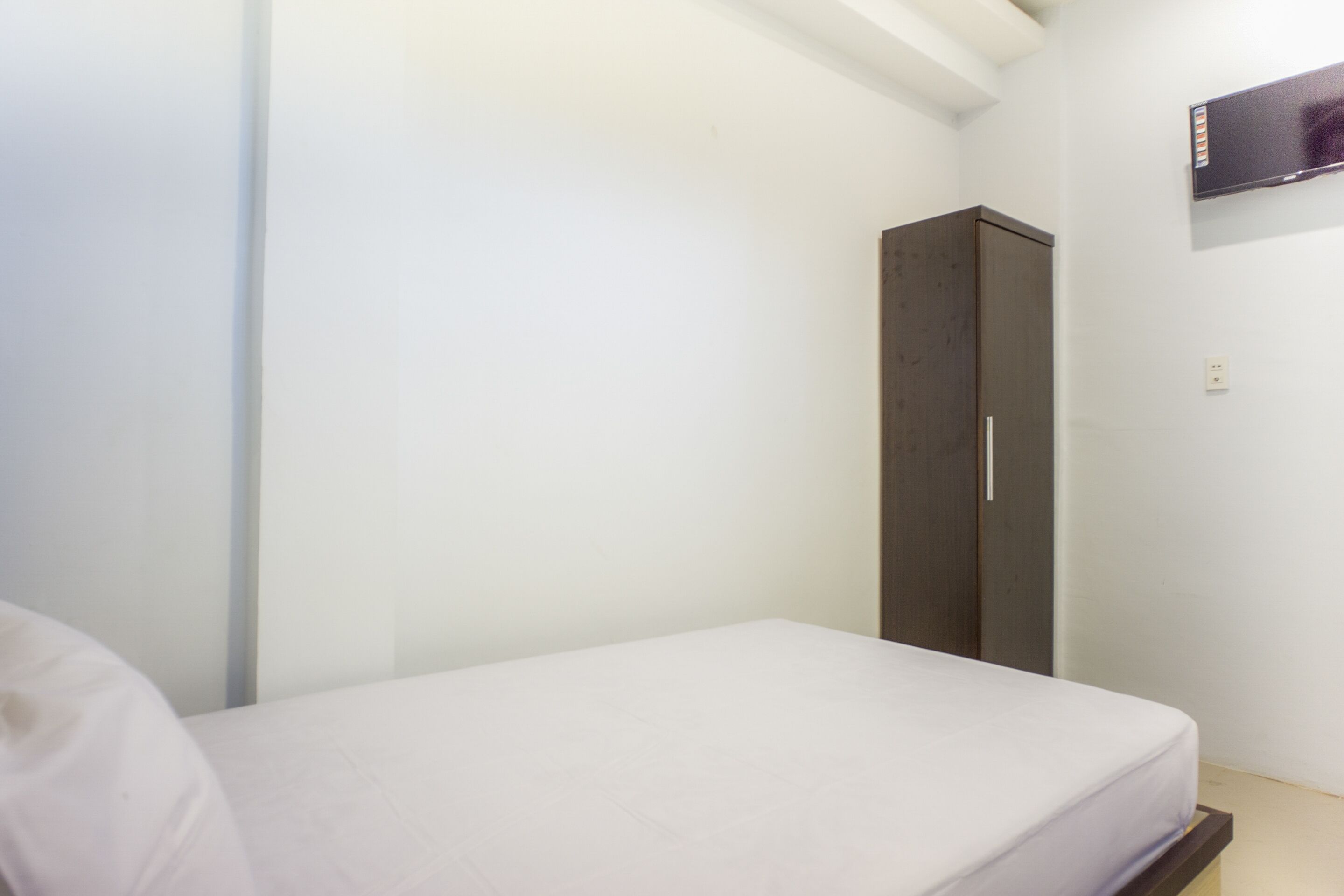 Une petite pièce, peu meublée, avec un lit simple, une armoire et un téléviseur fixé au mur.