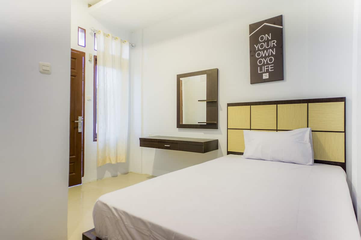 A hotel room with a bed, a bedside table, a mirror, and a wall-mounted sign.