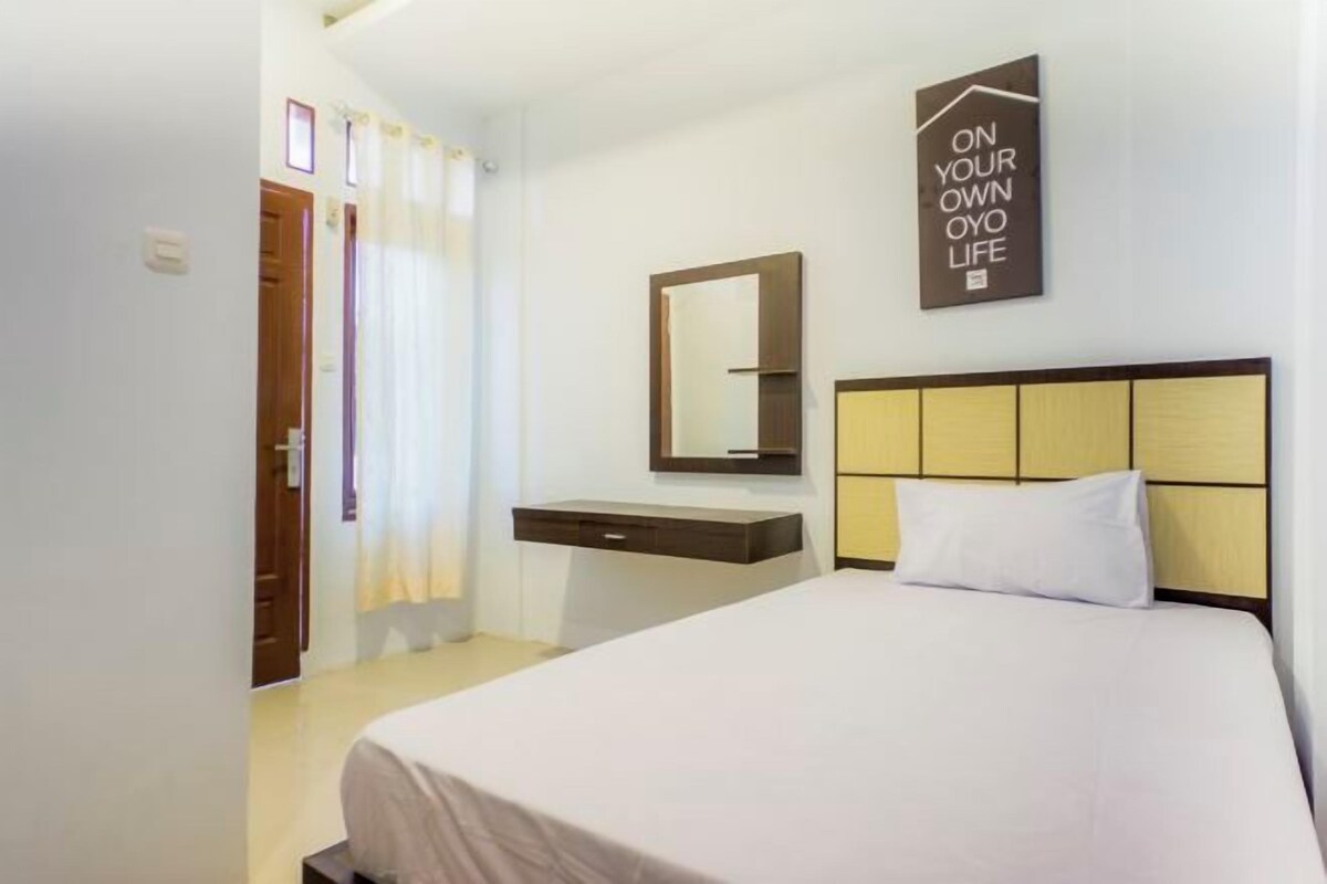 A hotel room with a bed, a bedside table, a mirror, and a wall-mounted sign.
