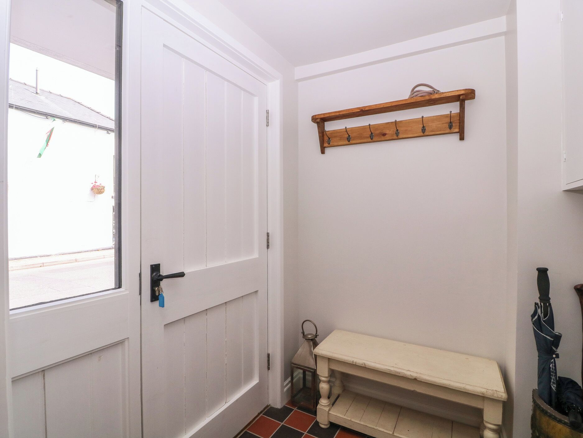 A hallway with a white door, a bench, a coat rack, and a window with a view of the street.
