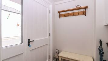 A hallway with a white door, a bench, a coat rack, and a window with a view of the street.