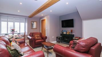 A living room with leather sofas, a coffee table, a fireplace, and a television mounted on the wall.