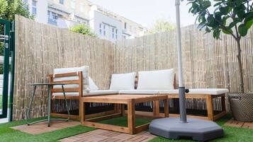 A wooden outdoor seating area with a bench and a table, surrounded by a bamboo fence and artificial grass.