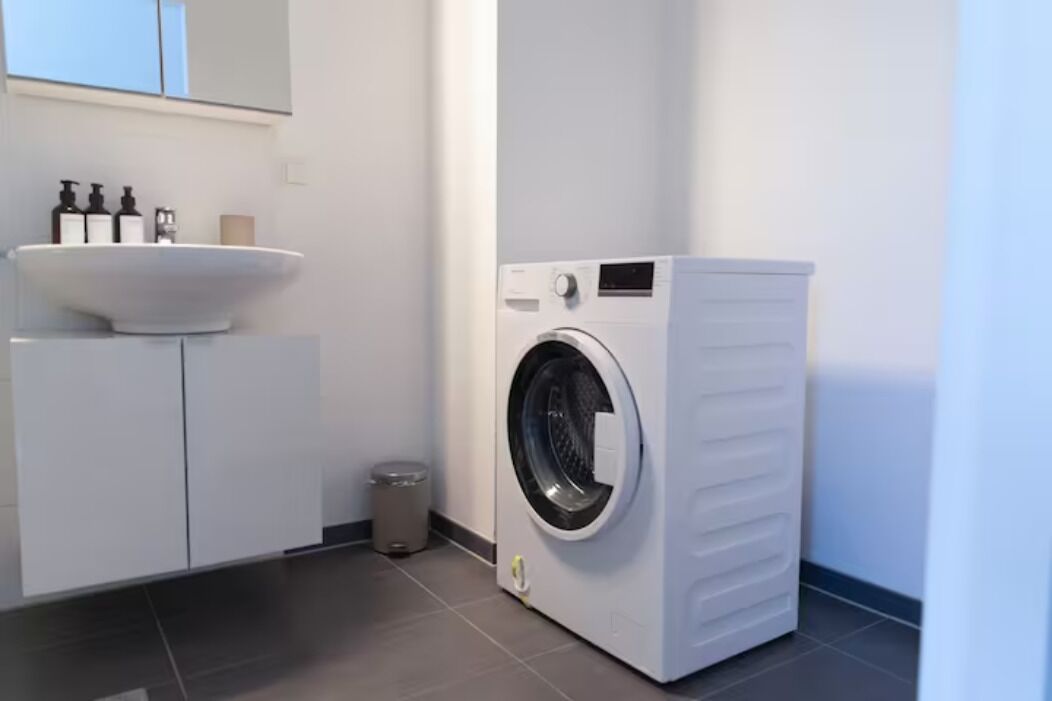 A modern bathroom with a built-in washing machine, a sink, and a trash bin.