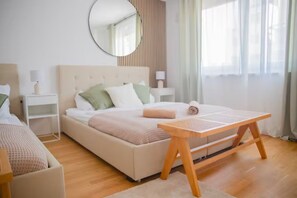 A modern hotel room with a large bed, bedside tables, a round mirror, and a wooden table.