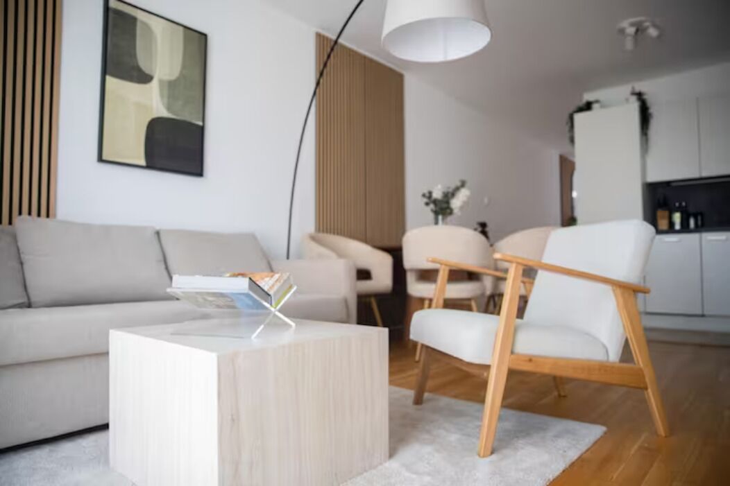 Ein modernes Wohnzimmer mit einer Couch, einem Couchtisch und einem Sessel. Im Hintergrund ist eine Küchenzeile zu sehen.