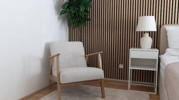 Een moderne slaapkamer met een wand van houten latten, een witte stoel, een nachtkastje met een lamp, en een bed met wit beddengoed.