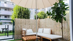 Une terrasse avec un banc en bois, un fauteuil et une table placés sous une tonnelle.