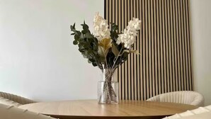 Une table ronde en bois sur laquelle est posé un vase en verre transparent contenant des fleurs blanches et des feuilles vertes.