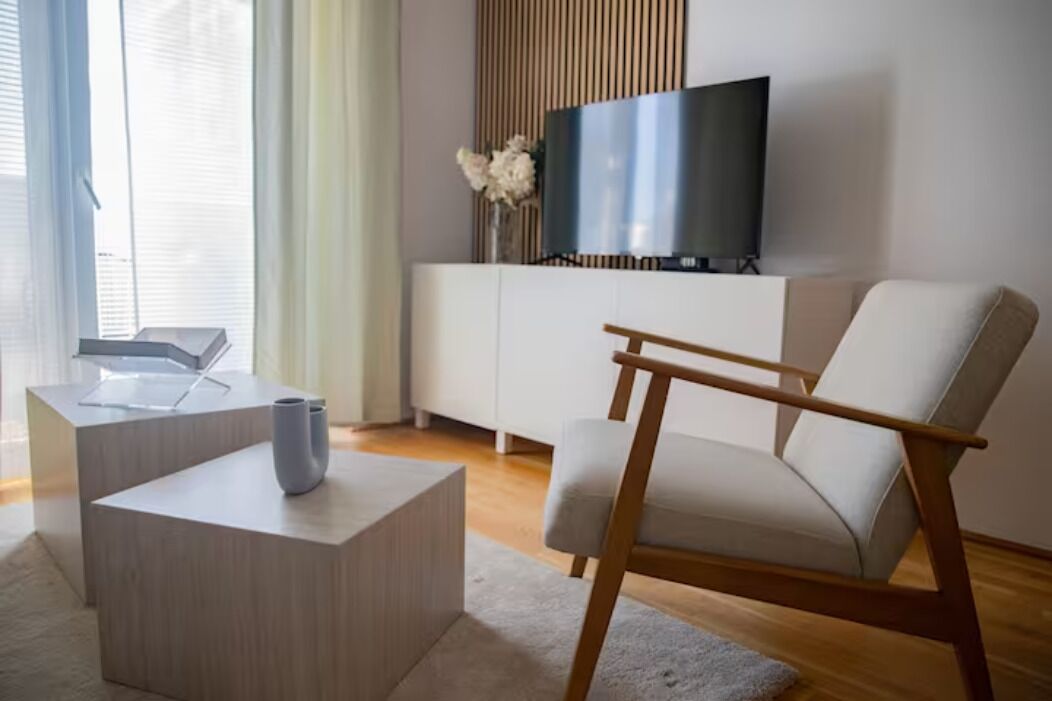 Un salon moderne avec un canapé blanc, une table basse en bois et un t éléviseur posé sur un meuble blanc.