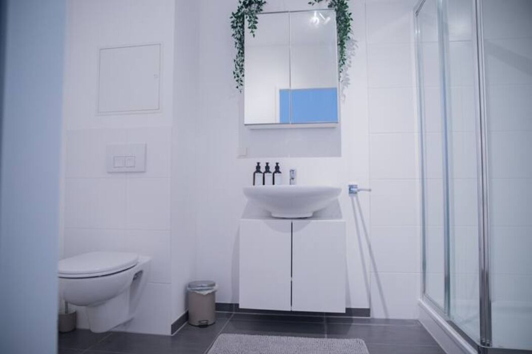 Un baño moderno con inodoro, un lavabo blanco con espejo y cabina de ducha.