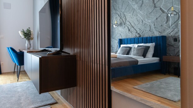 Une chambre moderne avec un lit bleu, un bureau en bois et un mur à la texture pierre.