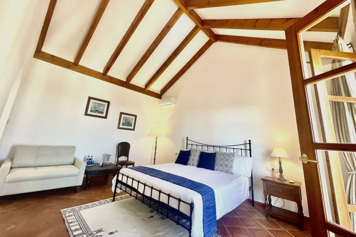 A bedroom with a bed, a chair, a desk, and a window.