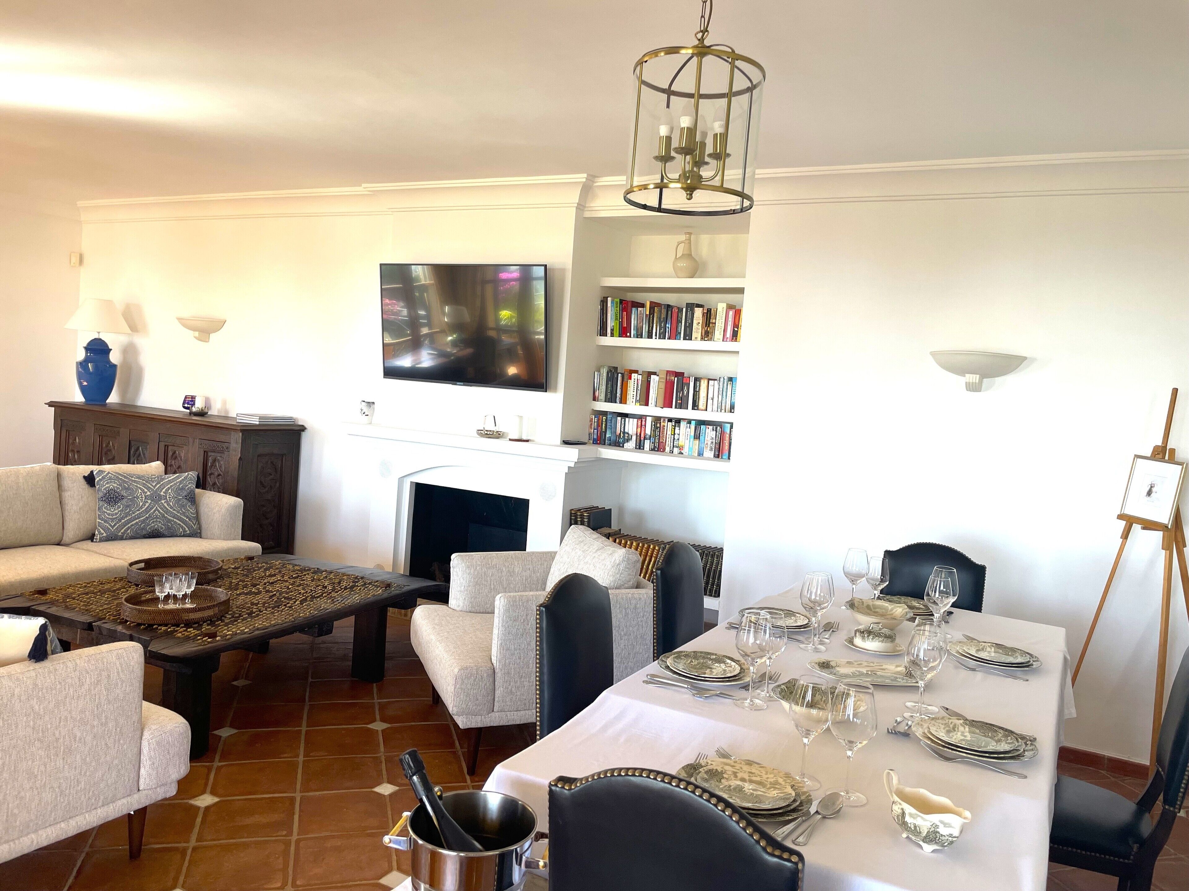 Un salon avec une cheminée, un téléviseur, une bibliothèque et un coin repas aménagé pour prendre un repas.