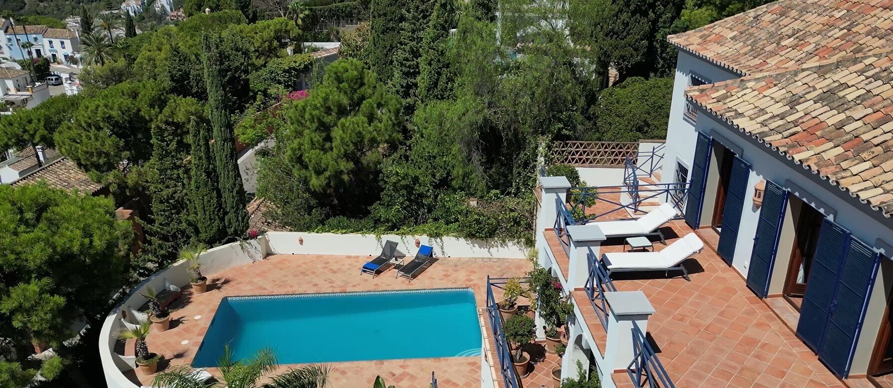 Una piscina sul tetto con sedie a sdraio, circondata da vegetazione ed edifici.