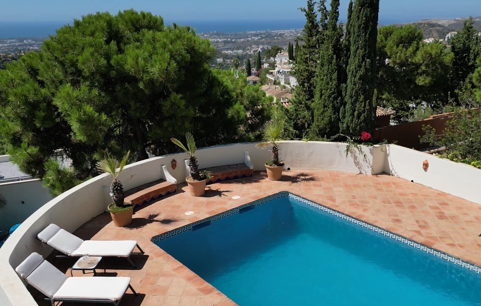 Uma piscina no terraço com vista para o mar, rodeada por plantas em vasos e móveis de exterior.