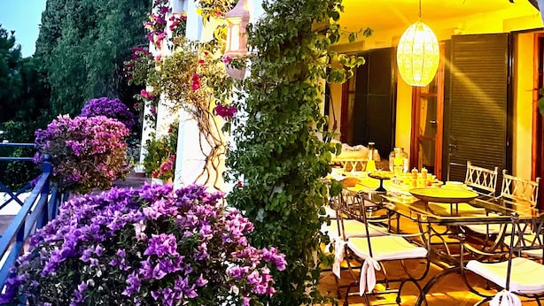 An outdoor seating area with tables and chairs, surrounded by potted plants and flowers.