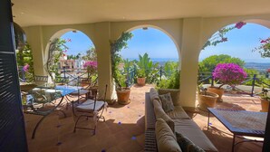 A covered outdoor patio with a seating area, potted plants, and a view of the sea.