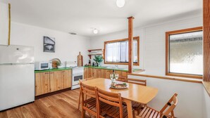Una cocina compacta con armarios de madera, una mesa de comedor y un ventanal con cortinas.