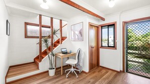Una oficina en casa con una escalera de madera, un escritorio con una computadora portátil, una silla y una planta en maceta.