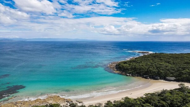 Un paisaje costero con una playa, aguas turquesas cristalinas y una zona boscosa.