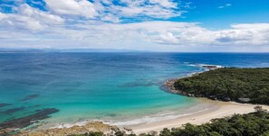 Un paisaje costero con una playa, aguas turquesas cristalinas y una zona boscosa.