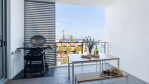 A balcony with a grill, a table with drinks, and a view of buildings and palm trees. - Blue Horizon on Manning (Kiama)